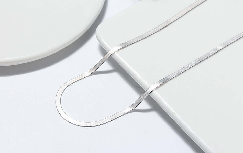 Close-up of a 3mm Sterling Silver Snake Bone Necklace laid on a minimalist plate, showcasing its elegant design and shine.