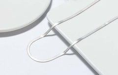 Close-up of a 3mm Sterling Silver Snake Bone Necklace laid on a minimalist plate, showcasing its elegant design and shine.